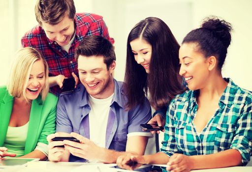 education, technology and internet - smiling students looking at smartphone at school