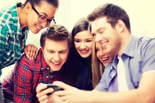 education and internet concept - smiling students looking at smartphone at school