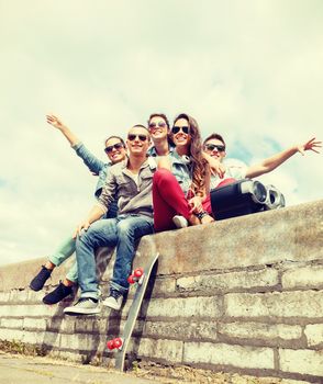 summer holidays and teenage concept - group of smiling teenagers with boob box and skatboard hanging out outside