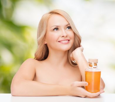 health and beauty concept - happy woman with oil bottle