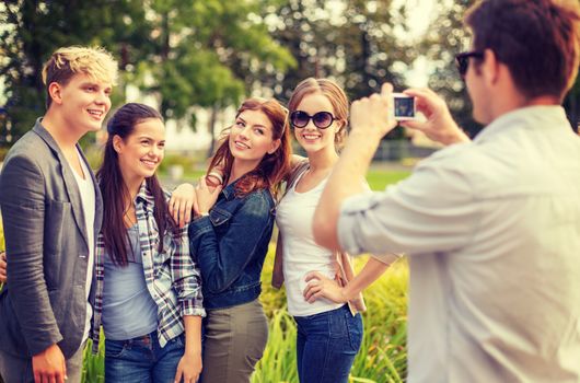 summer holidays, electronics and teenage concept - group of smiling teenagers taking photo with digital camera outside