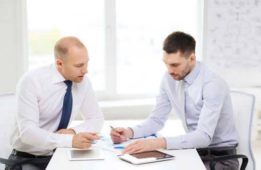 business, technology and office concept - two serious businessmen with tablet pc computers and files in office