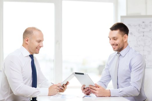 business, technology and office concept - two smiling businessmen with tablet pc computers and files in office