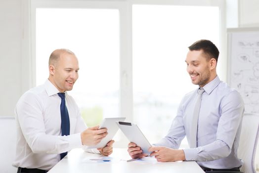 business, technology and office concept - two smiling businessmen with tablet pc computers and files in office