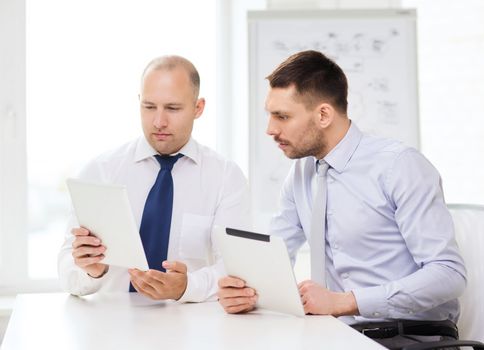 business, technology and office concept - two serious businessmen with tablet pc computers in office