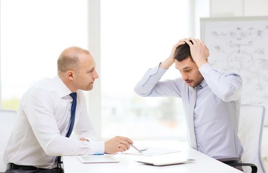 business, technology and office concept - two serious businessmen with tablet pc computers and files in office