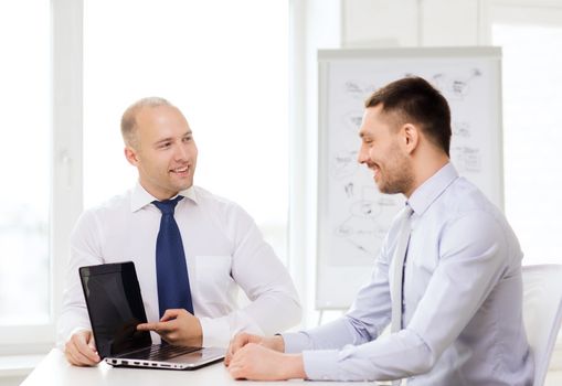 business, technology and office concept - two smiling businessmen with laptop having presentation in office