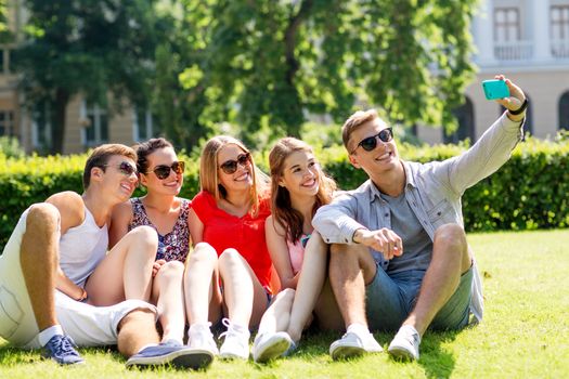 friendship, leisure, summer, technology and people concept - group of smiling friends with smartphone making selfie in park