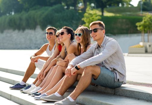 friendship, leisure, summer and people concept - group of smiling friends sitting on city square