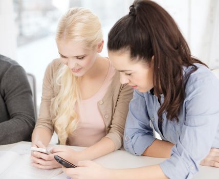 school, education, technology and internet concept - two teens with smartphones at school