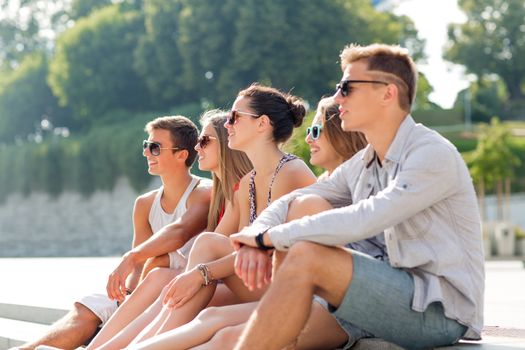 friendship, leisure, summer and people concept - group of smiling friends sitting on city square