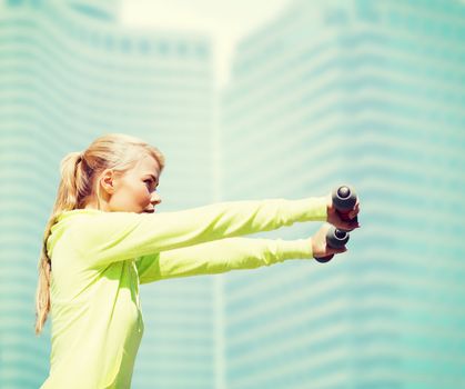 sport and lifestyle - young sporty woman with light dumbbells outdoors