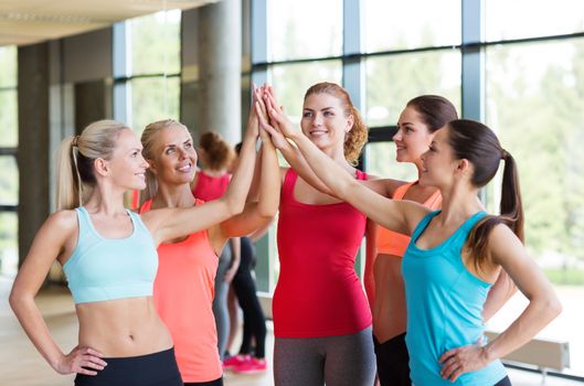 fitness, sport, friendship and lifestyle concept - group of women making high five gesture in gym