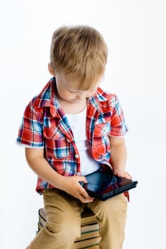 Little boy sitting on a pile of books with tablet computer