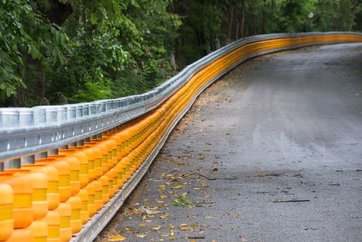 Yellow guard rail along a steep hill through a forest. Shallow depth of field with the foreground in focus.