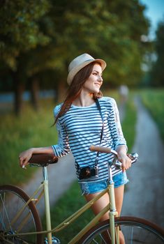 Lovely young woman in a hat with a bicycle in a park. Outdoors