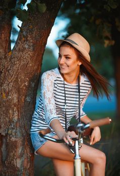Lovely young woman in a hat with a bicycle in a park. Outdoors