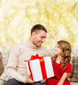 family, christmas, holidays and people concept -smiling father and daughter with gift box over yellow lights background