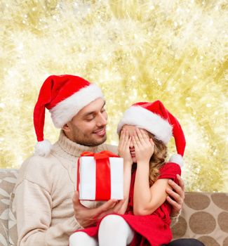 family, christmas, winter holidays and people concept - smiling daughter with closed eyes waiting for present from father over yellow lights background