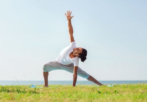 fitness, sport, people and lifestyle concept - smiling man making yoga exercises outdoors