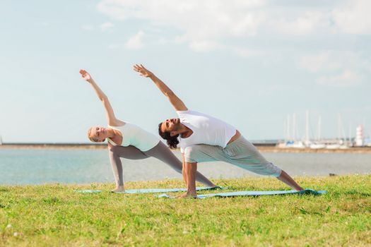 fitness, sport, friendship and lifestyle concept - smiling couple making yoga exercises on mats outdoors