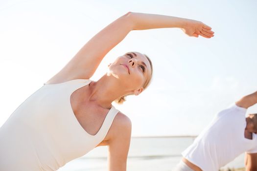 fitness, sport, friendship and lifestyle concept - close up of woman and man making yoga exercises on beach