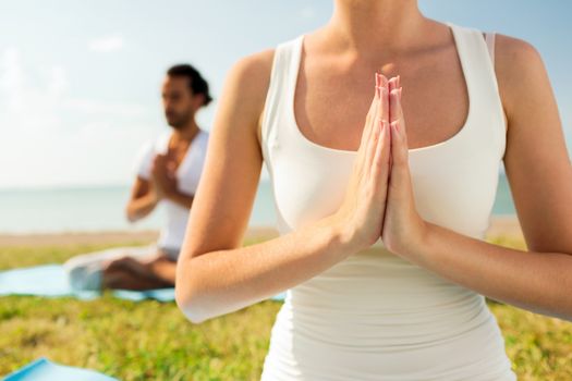 fitness, sport, people and lifestyle concept - close up of couple making yoga exercises sitting on mats outdoors