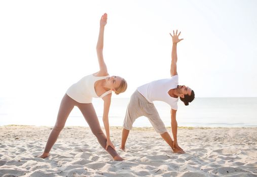 fitness, sport, friendship and lifestyle concept - couple making yoga exercises on beach