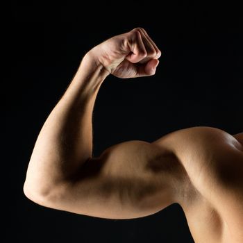 sport, bodybuilding, strength and people concept - close up of young man showing biceps over black background