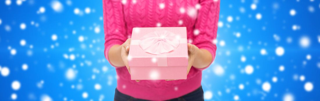 christmas, holidays and people concept - close up of woman in pink sweater holding gift box blue snowy background