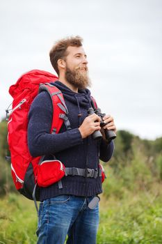 adventure, travel, tourism, hike and people concept - smiling man with red backpack and binocular outdoors