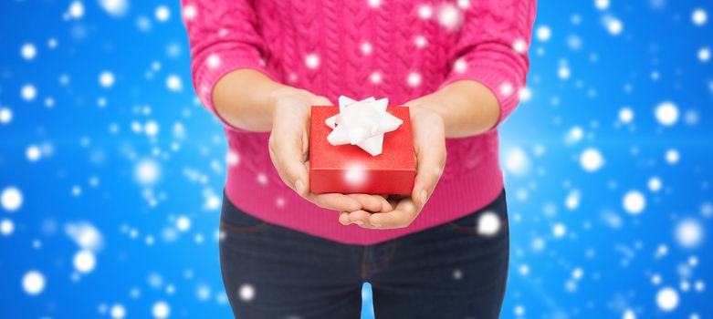 christmas, holidays and people concept - close up of woman in pink sweater holding gift box blue snowy background