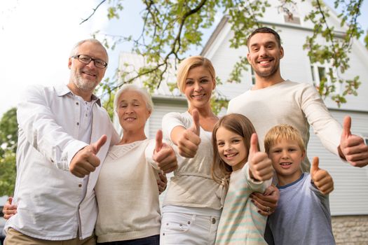 family, happiness, generation, home and people concept - happy family standing in front of house and showing thumbs up outdoors