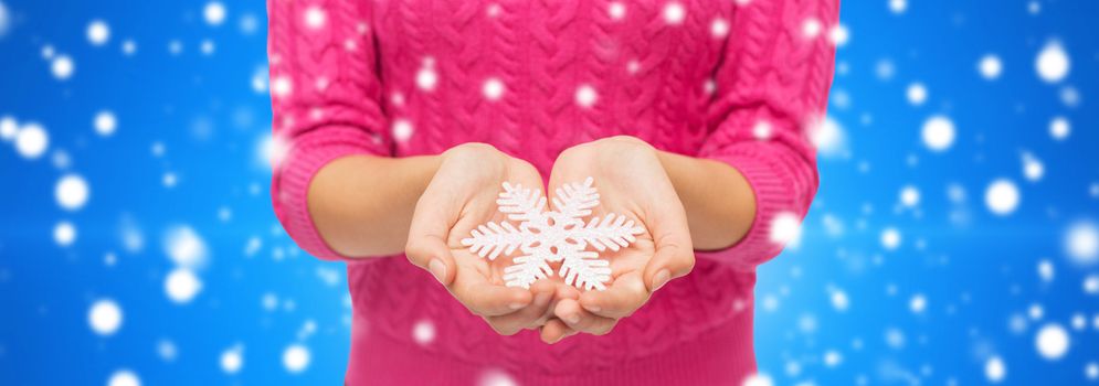 christmas, holidays and people concept - close up of woman in pink sweater holding snowflake blue snowy background