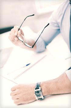 business, office, school and education concept - businessman with spectacles writing in notebook