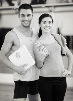 fitness, sport, training, gym and lifestyle concept - two smiling people with scale and water bottle in the gym