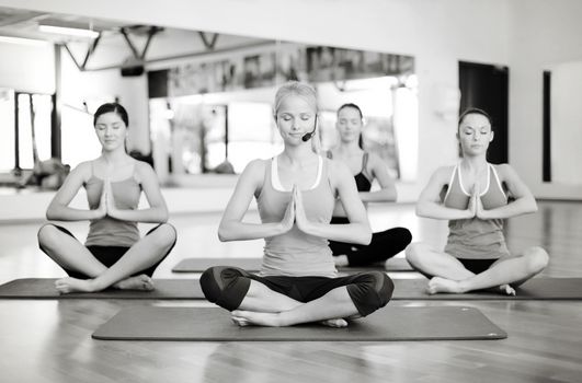 fitness, sport, training, gym and lifestyle concept - group of smiling women with trainer meditating in yoga pose