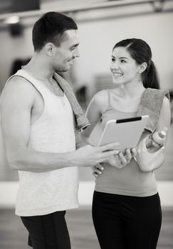 fitness, sport, training, gym, technology and lifestyle concept - two smiling people with tablet pc computer and water bottle in the gym