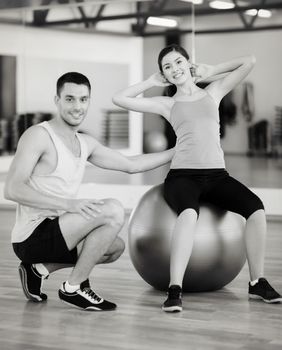 fitness, sport, training, gym and lifestyle concept - male trainer with woman doing crunches on the ball