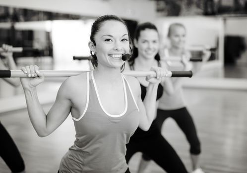 fitness, sport, training, gym and lifestyle concept - smiling trainer in front of the group of people working out with barbells in the gym