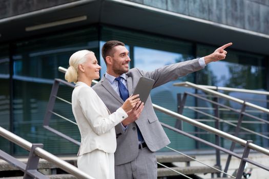 business, partnership, technology and people concept - smiling businessman and businesswoman with tablet pc computer over office building