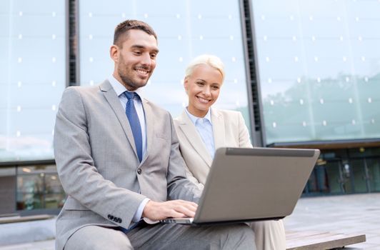 business, education, technology and people concept - smiling businesspeople working with laptop computer on city street