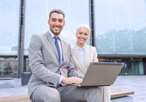 business, education, technology and people concept - smiling businesspeople working with laptop computer on city street