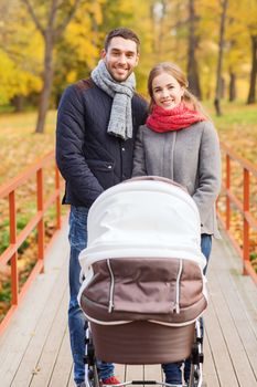 love, parenthood, family, season and people concept - smiling couple with baby pram in autumn park