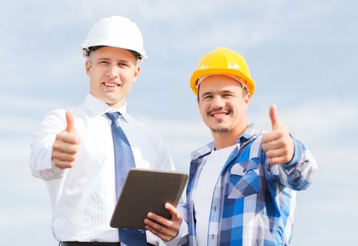 business, building, teamwork, technology and people concept - smiling builders in hardhats with tablet pc computer outdoors