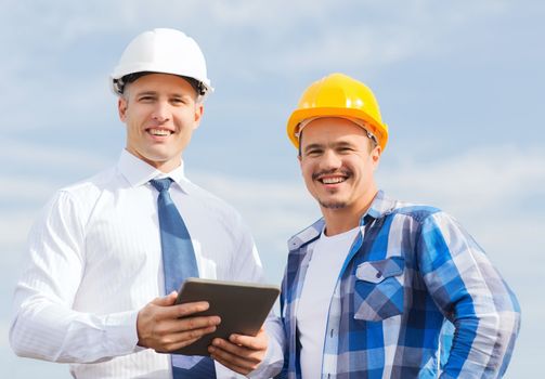 business, building, teamwork, technology and people concept - smiling builders in hardhats with tablet pc computer outdoors