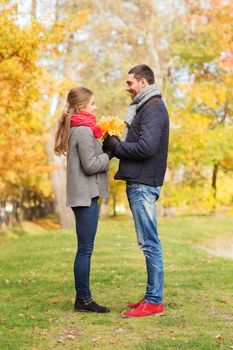 love, relationship, family, season and people concept - smiling couple with bunch of leaves in autumn park