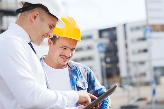 business, building, teamwork, technology and people concept - smiling builders in hardhats with tablet pc computer outdoors