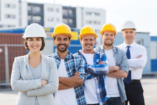 business, building, teamwork and people concept - group of smiling builders in hardhats outdoors