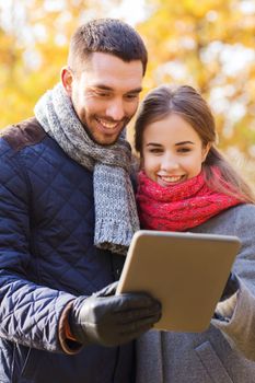 technology, relationship, family and people concept - smiling couple with tablet pc computer in autumn park